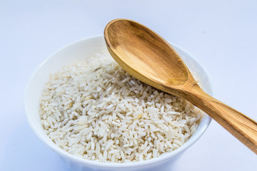 raw rice in white plate and wooden spoon, horizontal
