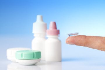 Contact lens on finger , case and bottle of solution 