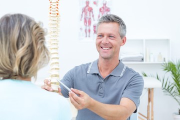Smiling physiotherapist showing spine model to his patient - Powered by Adobe
