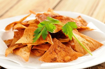 Fried triangle lavash chips in white plate with fresh parsley