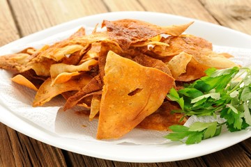 Fried triangle lavash chips in white plate with fresh parsley