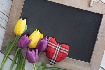 leere Kreidetafel mit Tulpen und kleinem Herz aus Stoff