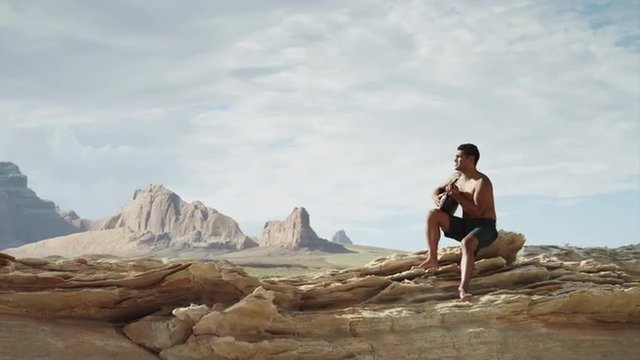 WS DS Man playing guitar on rocks near Lake Powell / Utah, USA