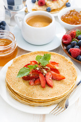 crepes with strawberries and honey on white wooden background