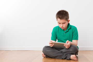 Serious Young Boy on the Floor Busy with Tablet