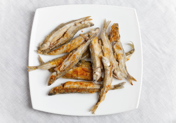 Pile of fried smelts fish lays on a white plate, top view