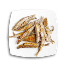Pile of fried smelts fish lays on a white plate, top view isolat