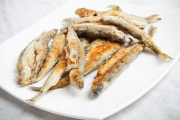 Pile of fried smelts fish lays on a white plate, closeup photo w