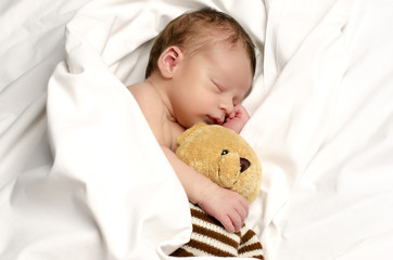 Little boy sleeping in white sheets after a bath with teddy bear