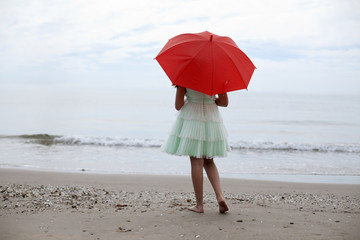 Niña con sombrilla roja de espaldas en la playa