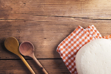 Lump of cheese on a cloth and two spoons laid on a wooden table 