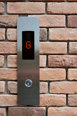 Elevator button down floor G on brick texture background.