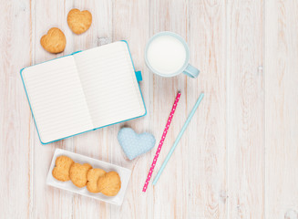 Fototapeta na wymiar Notepad, cup of milk, heart shaped cookies and gift toy