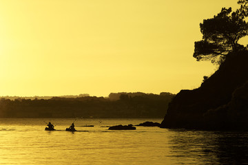 men sailing in kayak at sunset by the sea