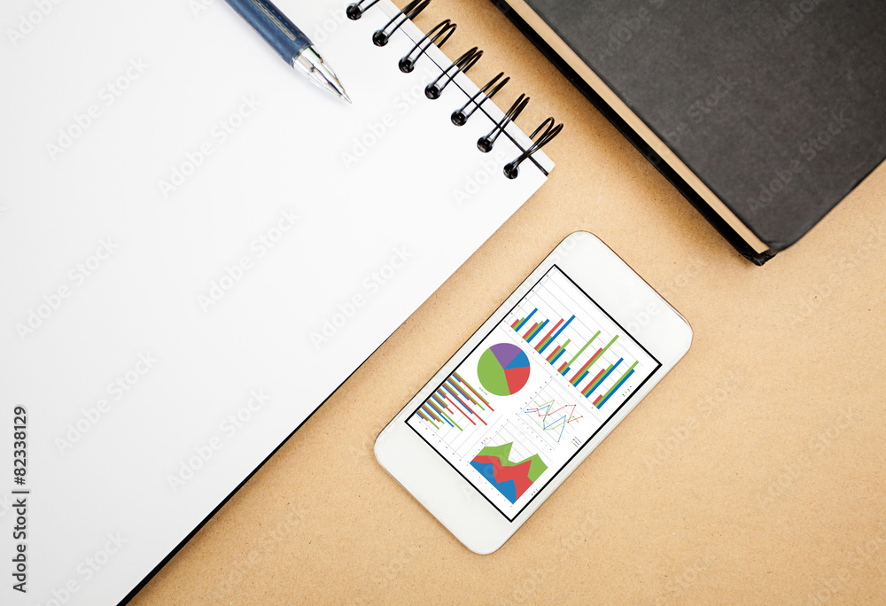Poster analyzing graph on smart phone with notebook on office table