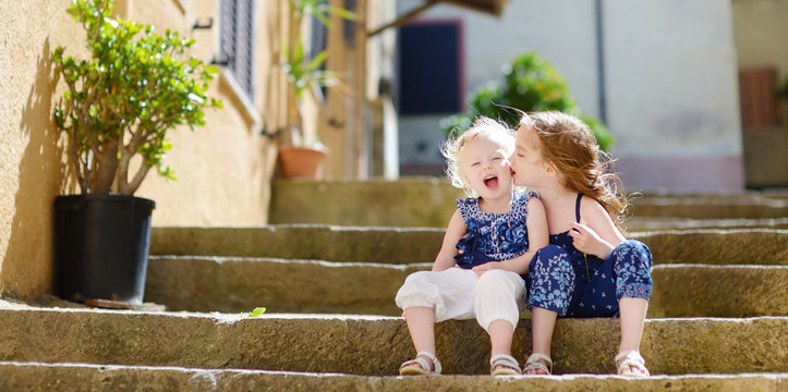 Two Kid Sisters Sitting On Stairs In Italian Town