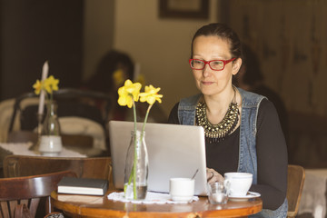 Young woman sitting with laptop at table in a cafe.
