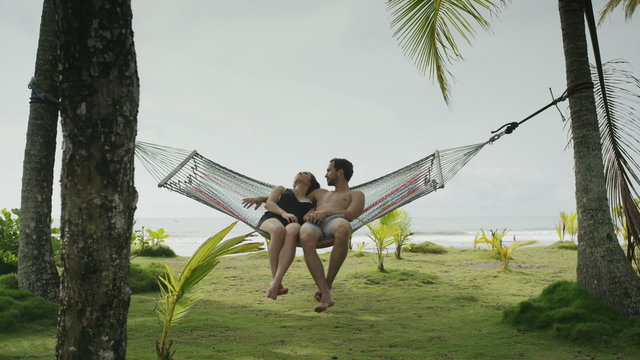 Slow motion panning wide shot of couple sitting in hammock / Esterillos, Puntarenas, Costa Rica
