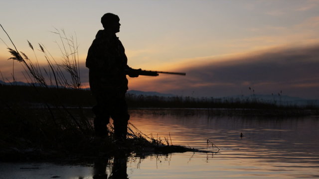silhouette of a duck hunter standing on the lake