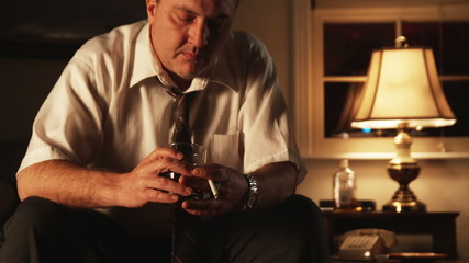 depressed man sitting in a motel room holding a drink and a cigarette