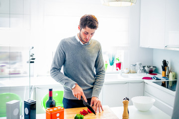 Handsome young man cooking at home cutting vegetables