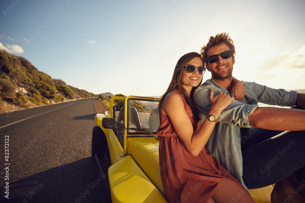 Wall mural Attractive young couple sitting on the hood of their car