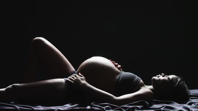 WS ZI MS Studio shot of pregnant woman lying against black background
