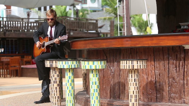 bearded man plays guitar sensually by bar counter