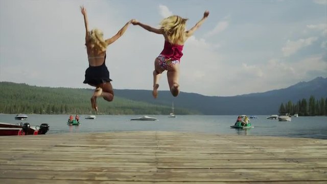 Slow motion medium shot of young women running from dock into lake / Redfish Lake, Idaho, United States