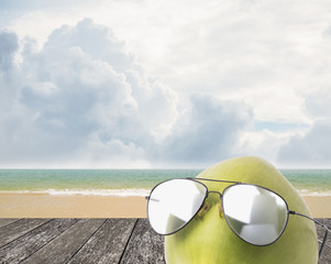 Fototapeta na wymiar Coconut wear sunglasses beside beach, Summer concept