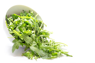 rocket salad leaves, rucola or arugula, falling from a ceramic b