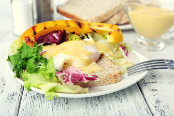 Toast with egg Benedict and greens on plate on wooden table