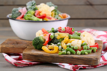Frozen vegetables on cutting board, on napkin, on wooden table background