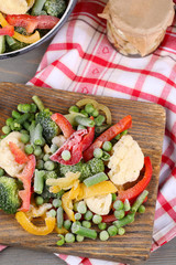 Frozen vegetables on cutting board, on napkin, on wooden table background