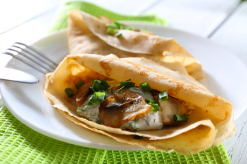 Pancakes with creamy mushrooms and greens in plate on wooden table, closeup