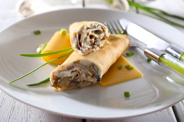 Pancakes with cream and mushrooms on wooden table, closeup