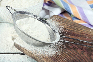 Sifting flour through sieve on wooden table, closeup
