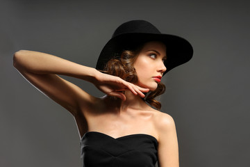 Portrait of beautiful model in black dress and hat on gray background