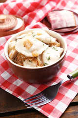 Tasty dumplings with fried onion in brown bowl, on wooden background