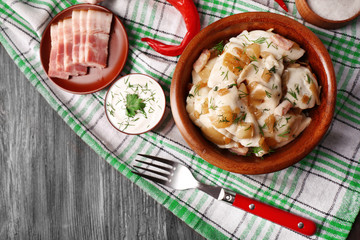 Fried dumplings with onion and bacon in frying pan, on wooden table background