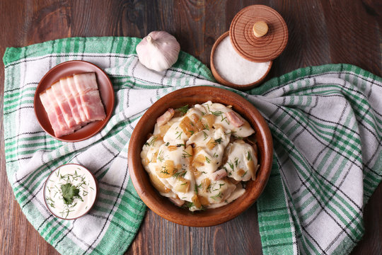 Fried dumplings with onion and bacon in frying pan, on wooden table background