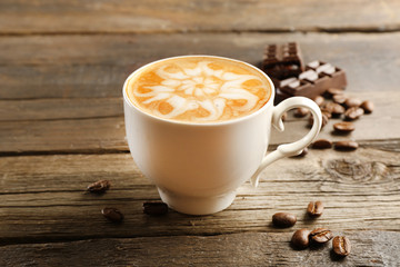 Cup of coffee latte art with grains and chocolate on wooden background