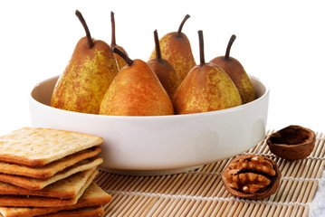 Yellow ripe pears in a white bowl with a walnut and crackers
