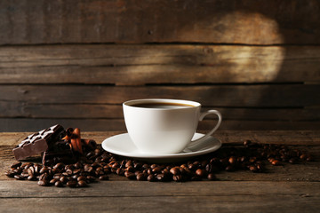 Cup of coffee with grains and chocolate on wooden background