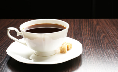 Cup of coffee with lump sugar on wooden table, on dark background