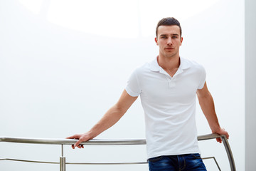 Man in a polo shirt stands leaning on railing