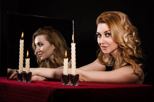 Beautiful young woman with candles near the mirror