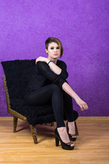 Girl with short haircut in a chair on a purple background