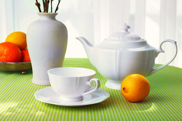 Willow twigs, teapot, cups and citrus on table on curtains background
