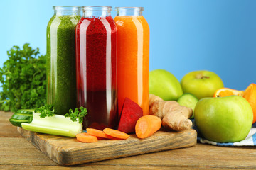 Assortment of healthy fresh juices in glass bottles on wooden table, on blue background